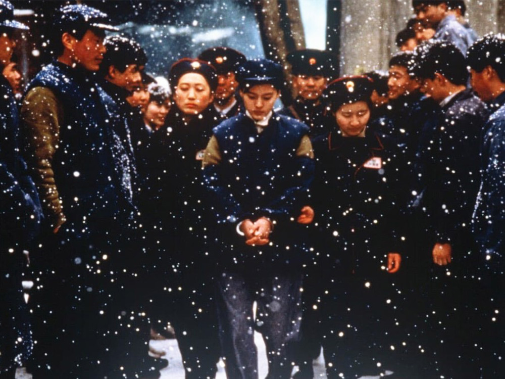 A person in a blue military outfit is led through the snow, hands tied