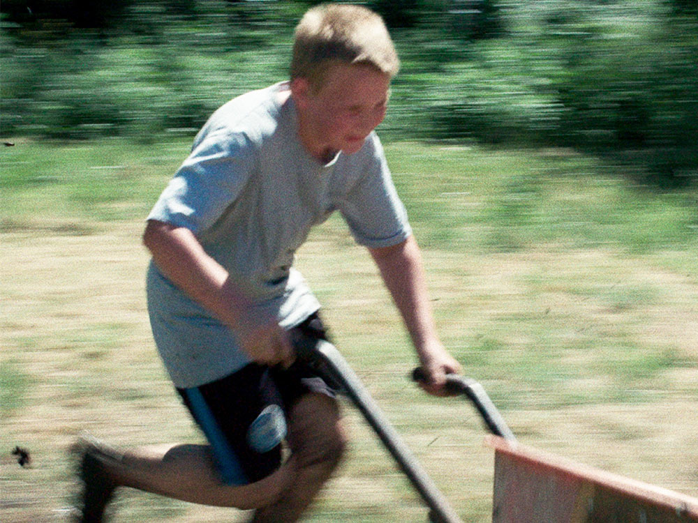 Happy boy pushing wheelbarrow in field