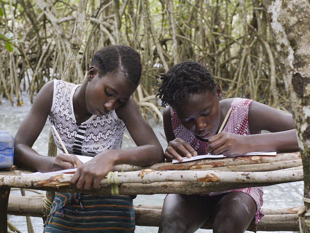 Two Black girls do homework on table made of tree branches