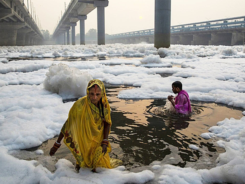 Two people in bright garbs wade through icy water below a concrete overpass