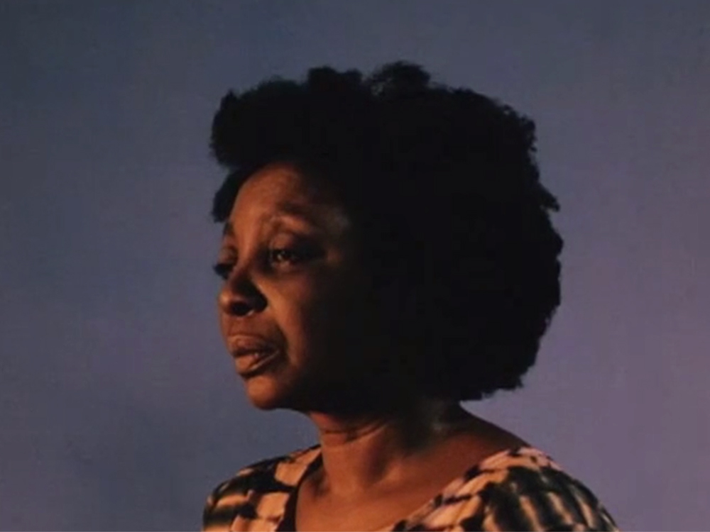 Side profile of a woman with an afro hairstyle, a longing and peaceful expression, against a gradient purple background