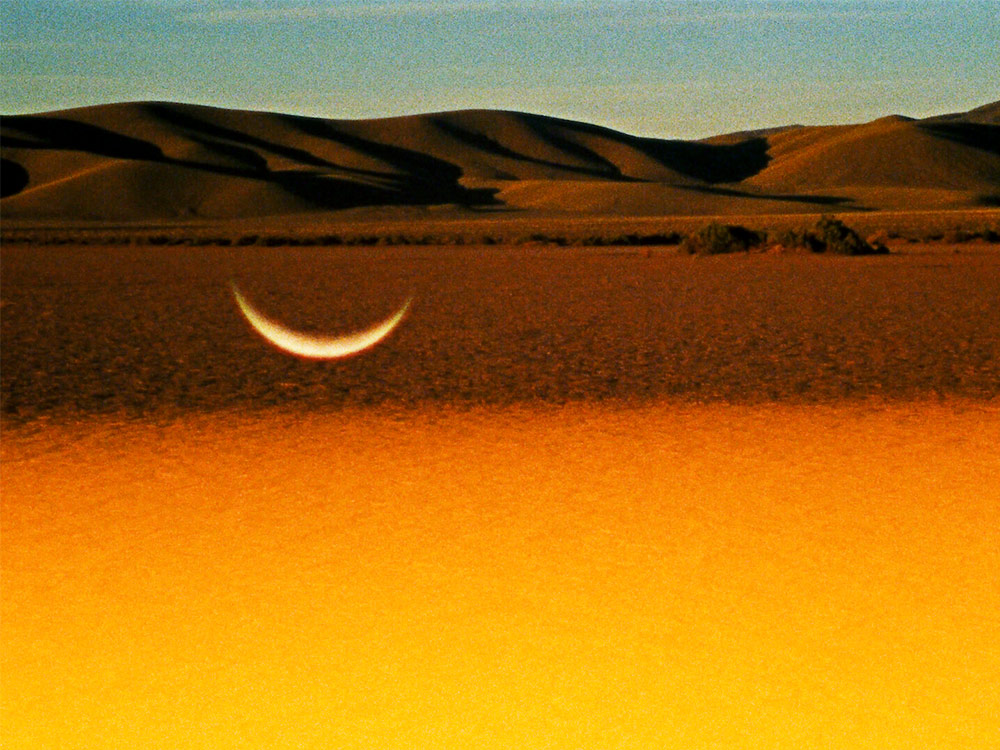 A crescent moon hanging downwards reflects over a bright orange desert
