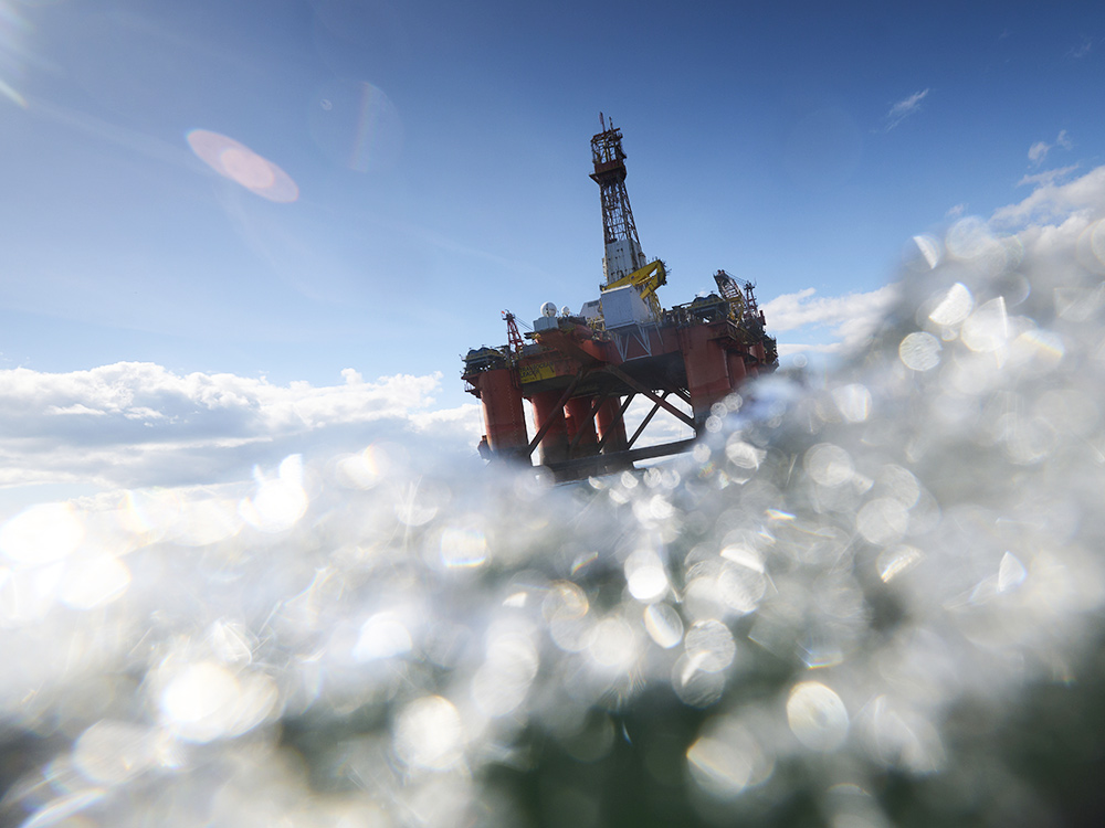 An oil rig floats above a rough ocean in bright sunlight.