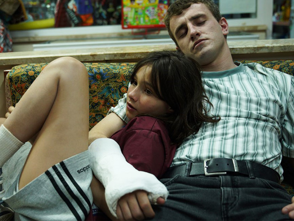 A young girl lays against a young man in an arm cast, resting on a couch