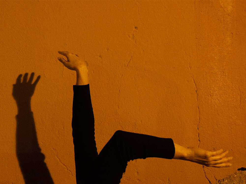 Two arms moving in angles against a concrete wall in orange light