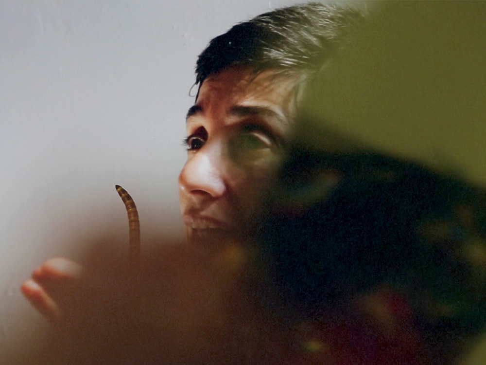 A person with short hair stares intensely into the distance. Their face is obscured by a blurred figure