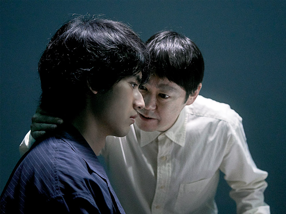 A person with a bowl haircut leans closely into someone's ear, whispering dark secrets