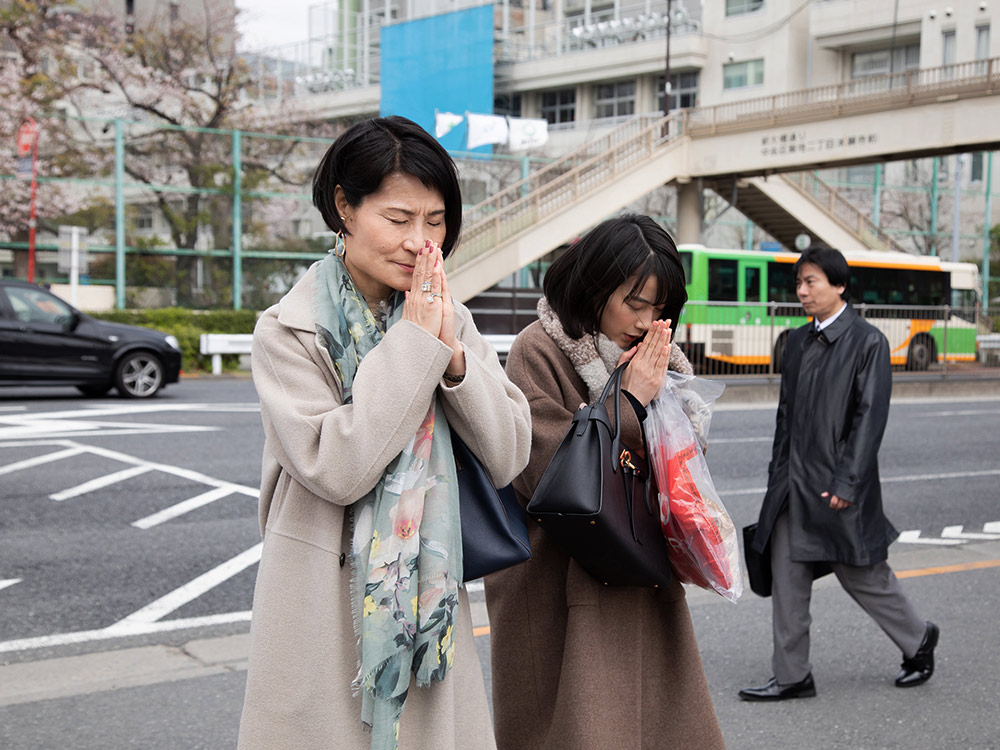 A younger person and an older person say prayers on a street in Tokyo