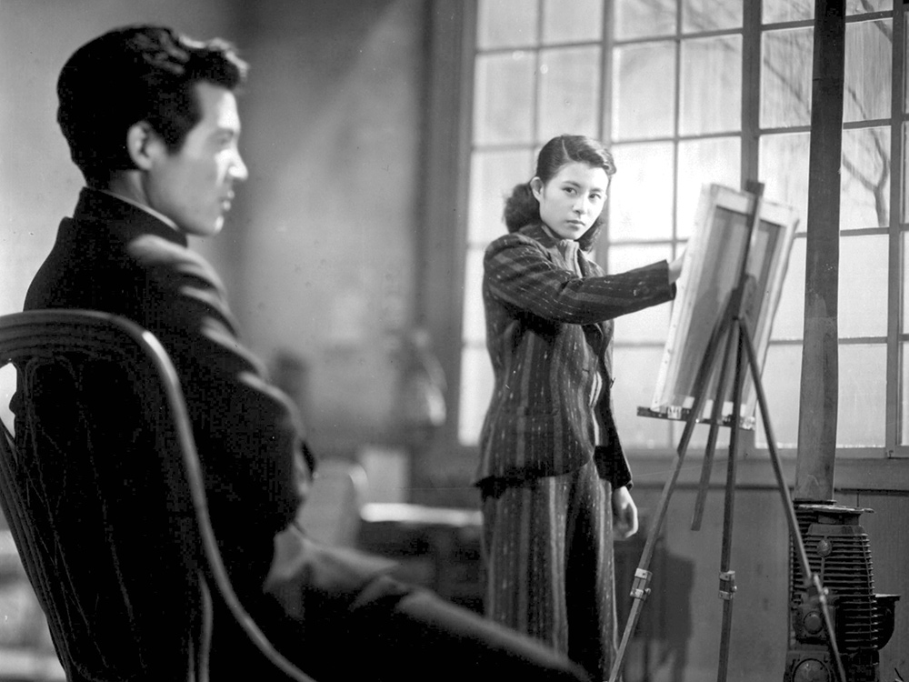 A young person in a suit sketches a portrait of their lover