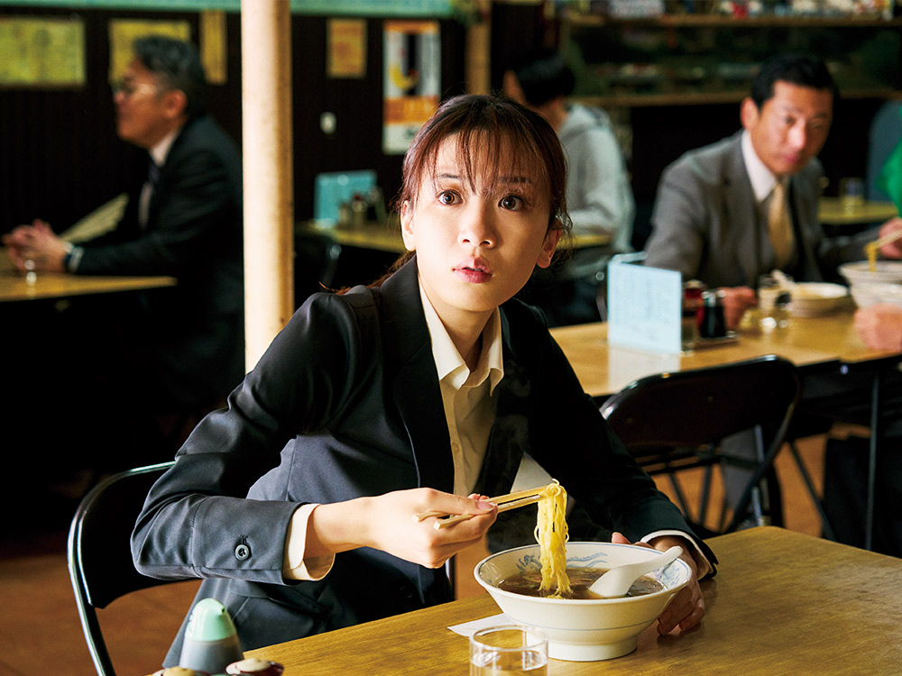 A person in business attire looks shocked while they eat a bowl of ramyun in a restaurant