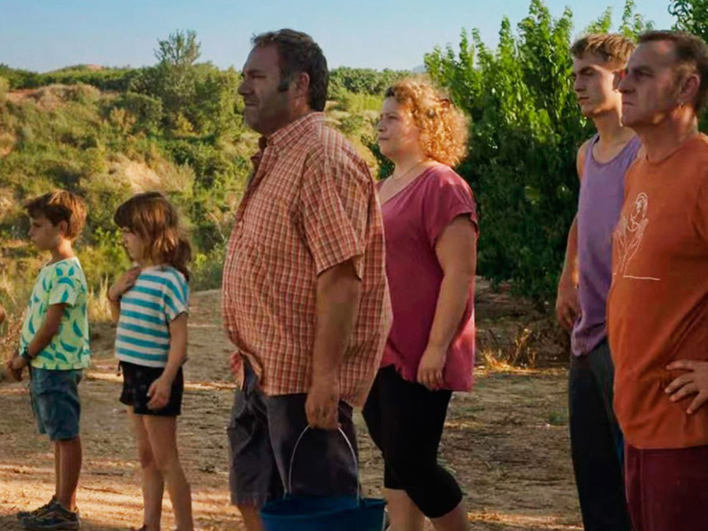 A family of many generations look out to a sadness in the distance. Their peach trees lie in the background