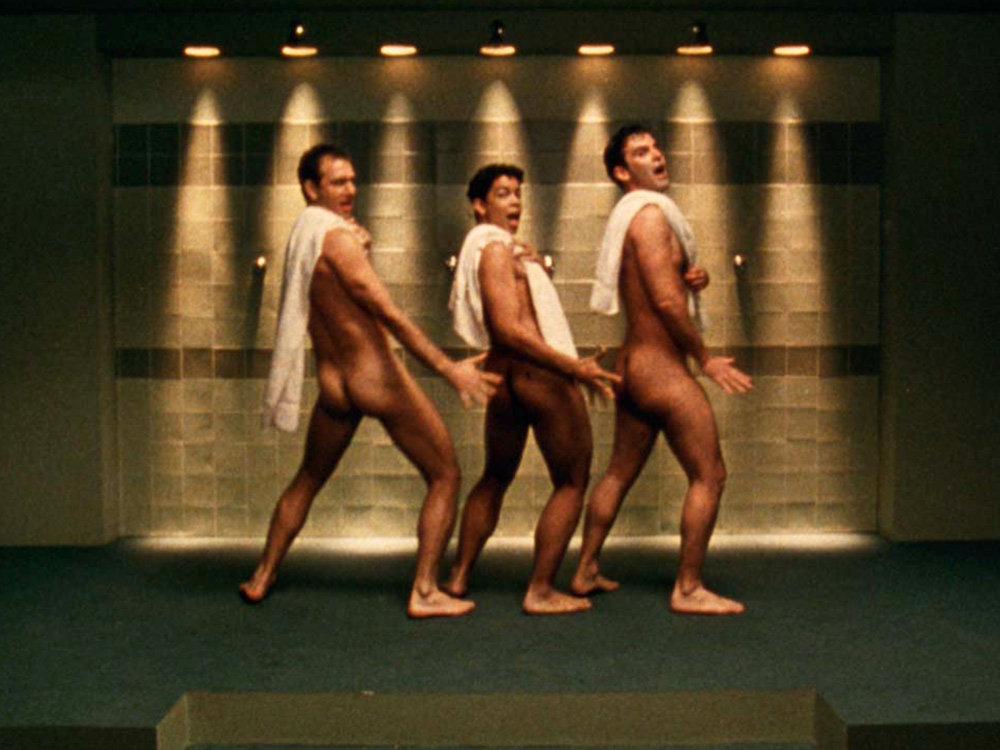 Three named men standing and posing in song at a public shower. They look like they're on stage in a musical