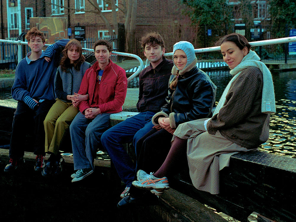 A photo of the band Black Country, New Road casually sitting by a canal in London