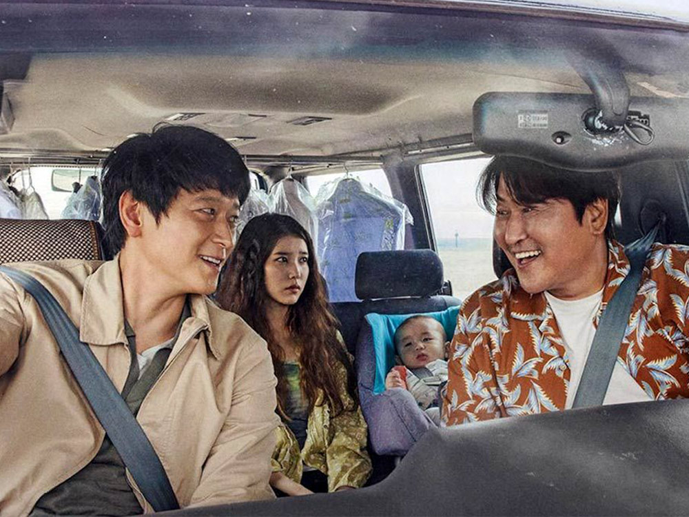 A trio of people and a baby are crammed in a car stuffed with drycleaning, looking happy