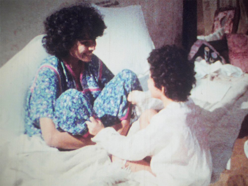 On old photo paper, a mother and child stare at each other with joy on their home sofa