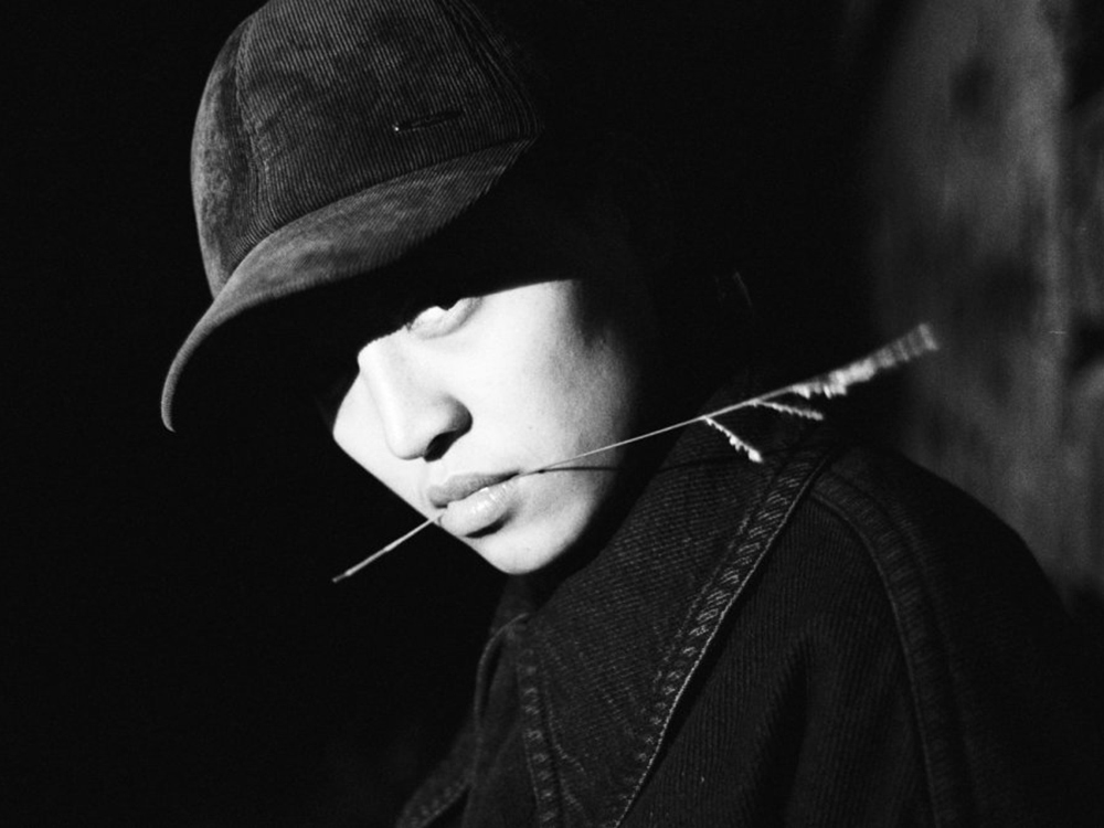 Pan Daijing faces the camera, wearing a corduroy cap, with a piece of wheat between her lips