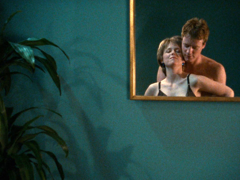 In pastel tones, in the corner, a square mirror lies against a wall with a pot plant. A client holds a sex worker from behind, reflected in the mirror