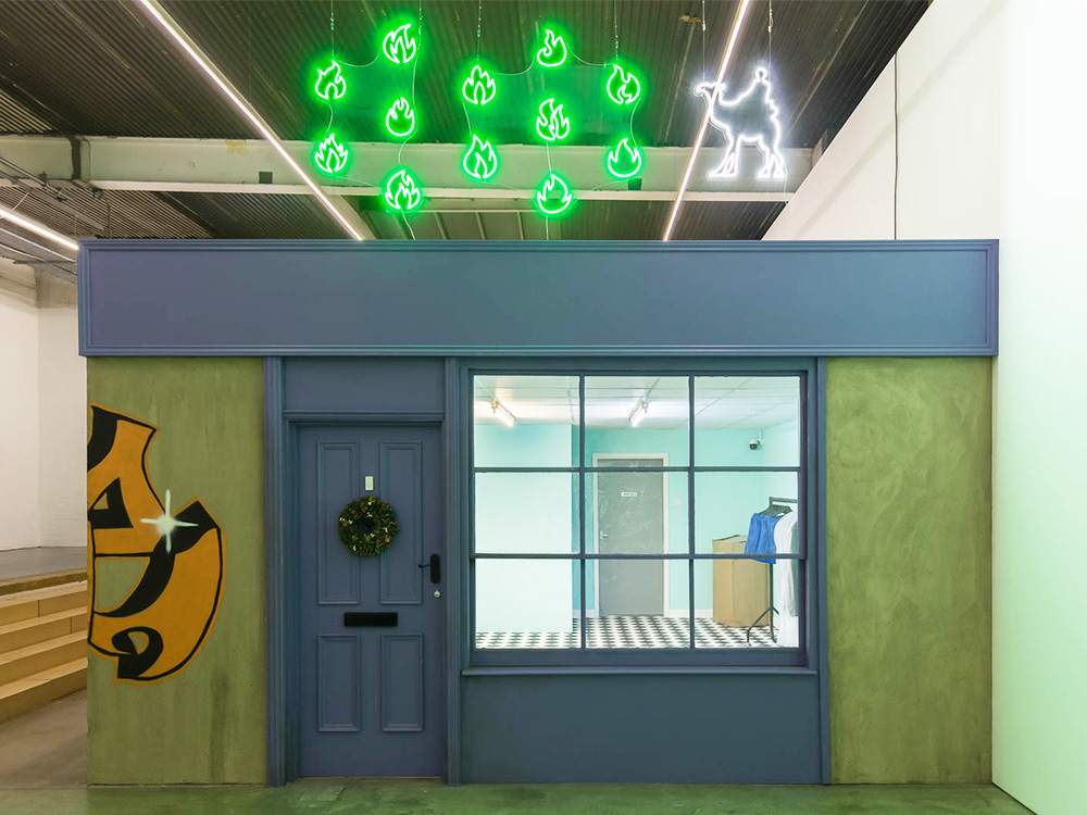 A shopfront in a gallery space, with neon signs hanging above