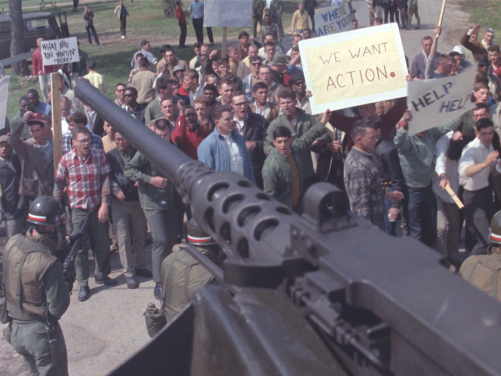 A huge artillery gun is flanked by riot police, overlooking a staged protest