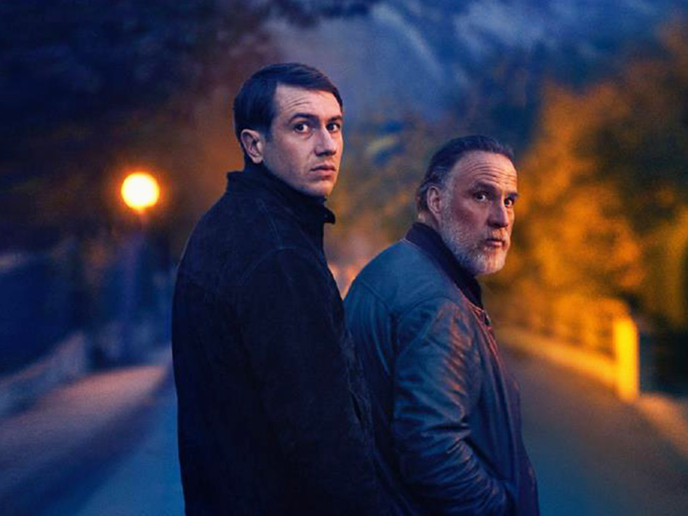 Two men look back in slight shock, standing on a dark street