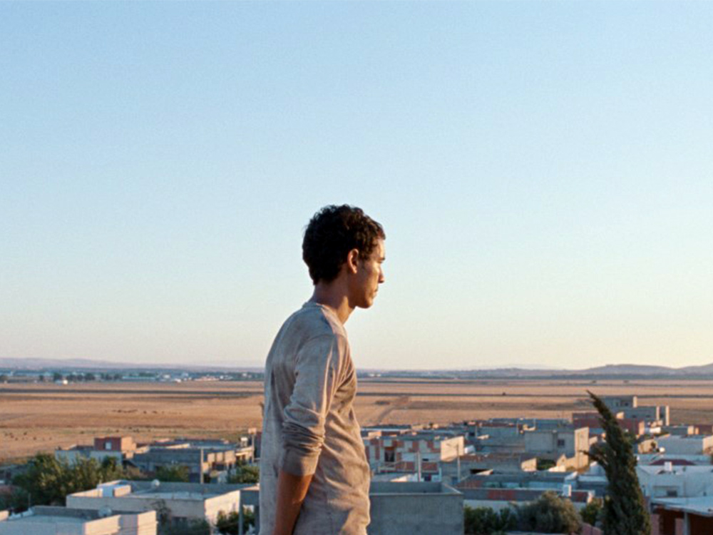 A person stands at the top of a city, overlooking a vast plain and light sunlight
