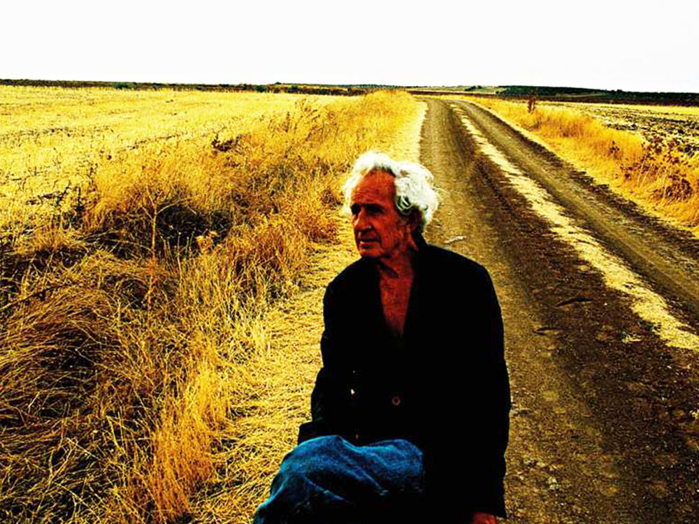 Albert Serra walks down a road beside a field of golden grass
