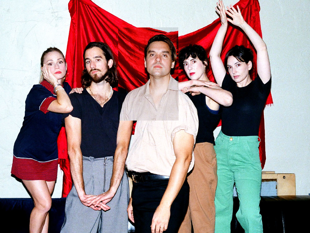 An image of Will Butler and the group Sister Squares. They stand loosely in front of a red velvet curtain hanging on the wall. Will's face is stuck onto the image like a photo