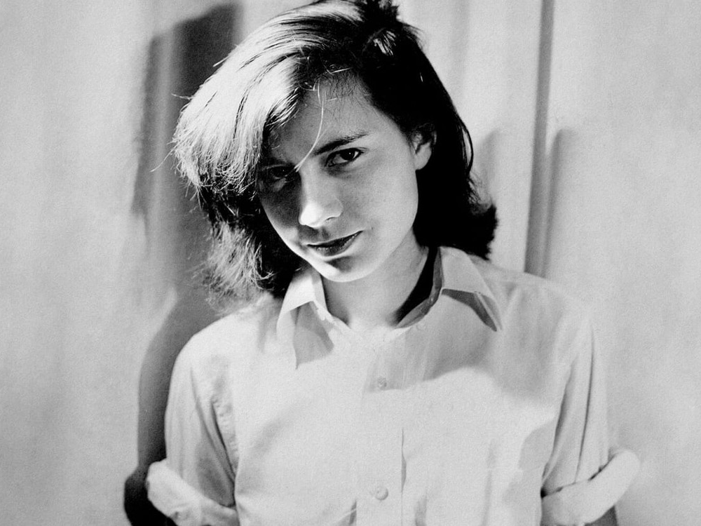 A black and white photo portrait of a young Patricia Highsmith, wearing a white blouse with rolled-up sleeves