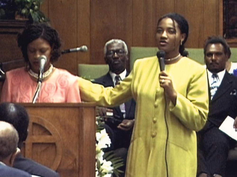 A black woman stands and delivers an address at a funeral