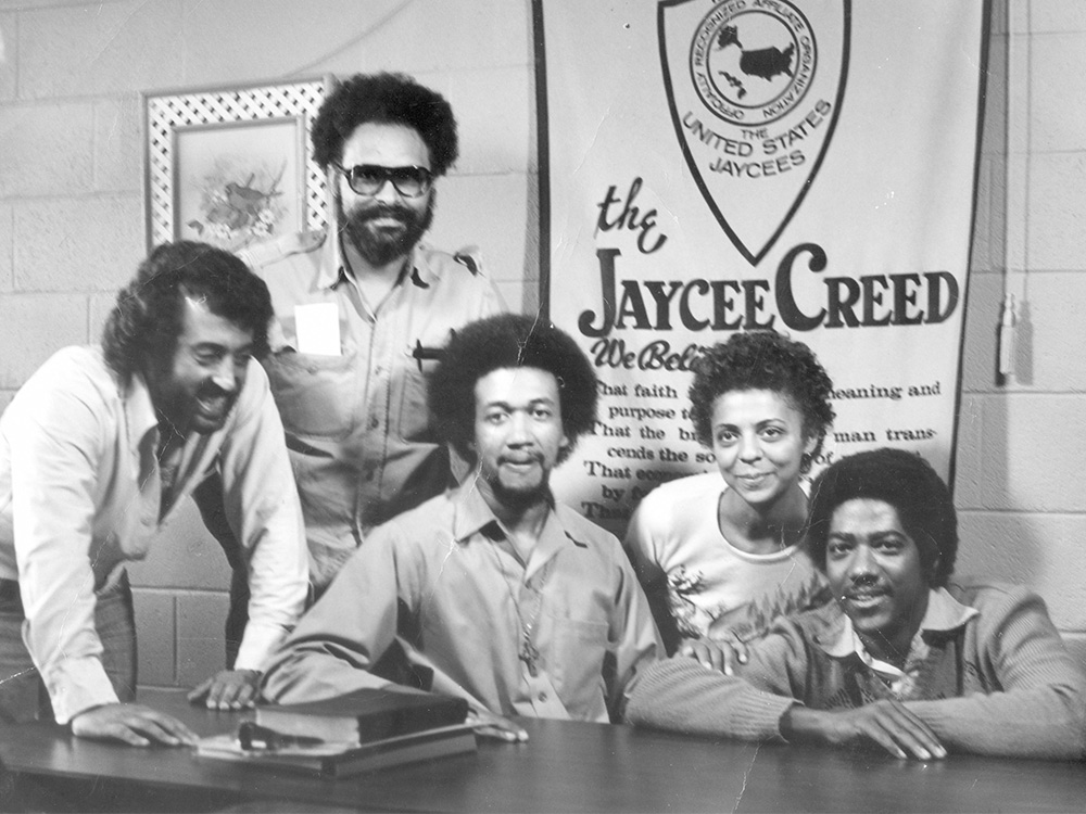 A group of black men and women sit at a desk in froot of a banner that reads 'The Jaycee Creed'