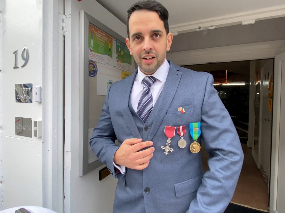 A man in a blue suit looks at the camera, badges pinned to his chest