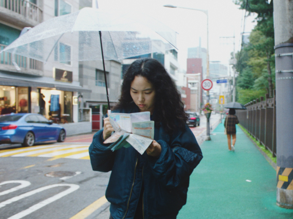 A young Korean woman reads a map while she stands on a quiet street of Seoul, under a clear umbrella