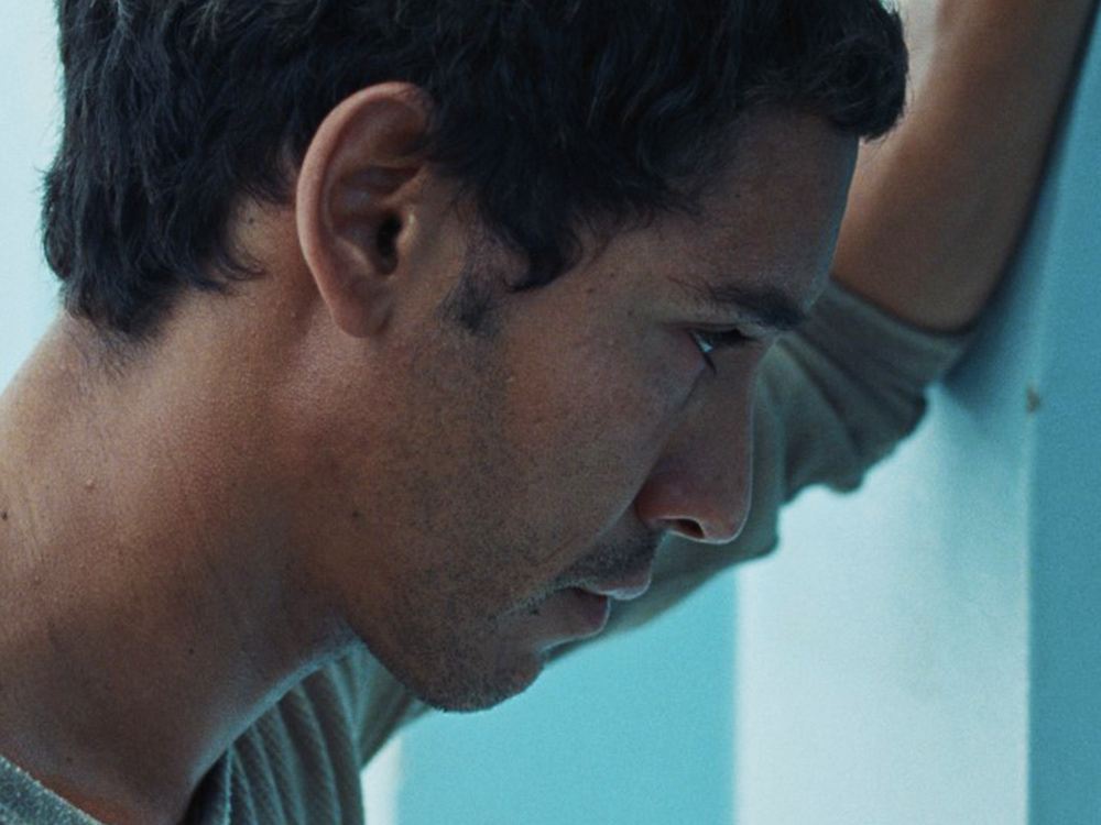 A young Tunisian man rests his arm against a light blue wall, staring quietly at the wall