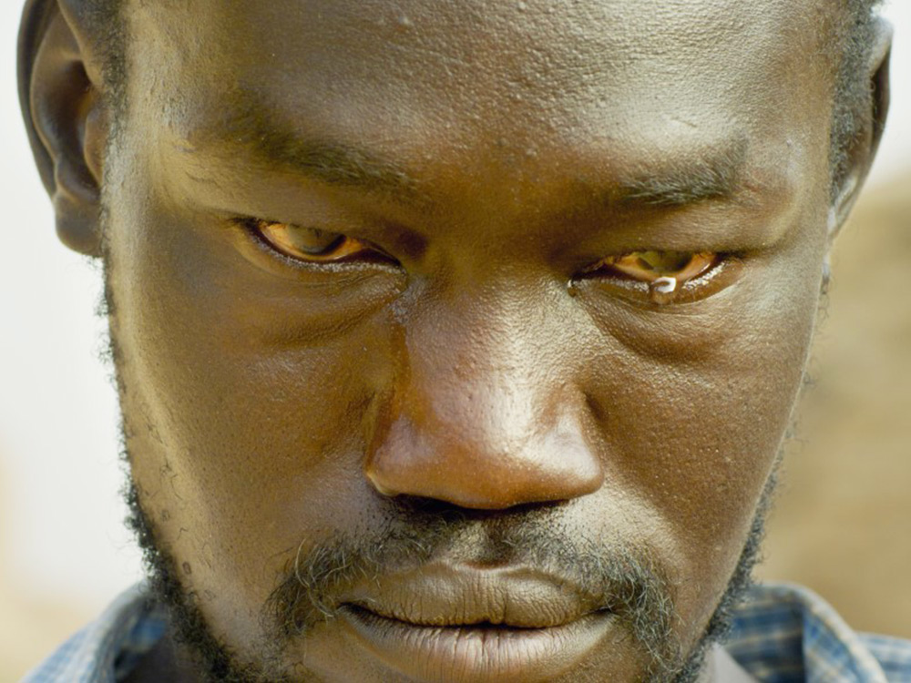 A black man stares at the camera, his eyes veiny and red, a single tear welling