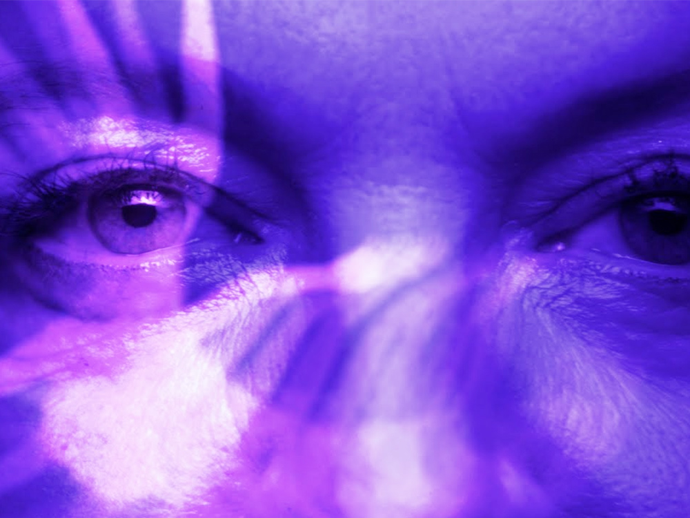 A super close-up set of eyes doused in purple light, with images transposed over the top