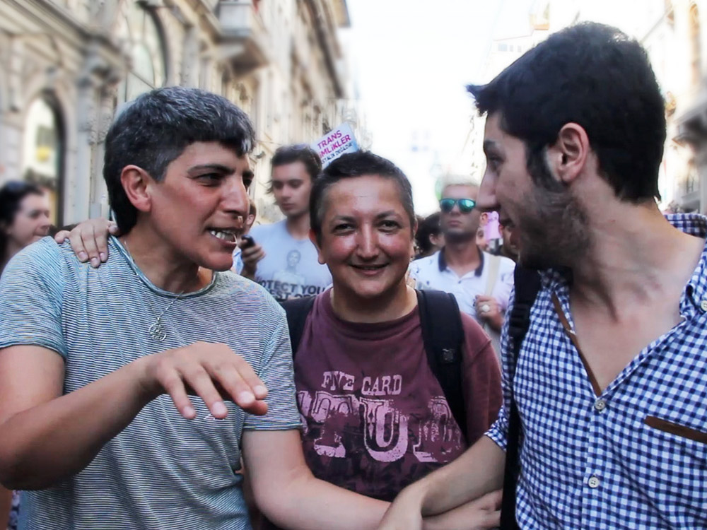 Three men walk at a trans rally together in Turkey, looking joyful