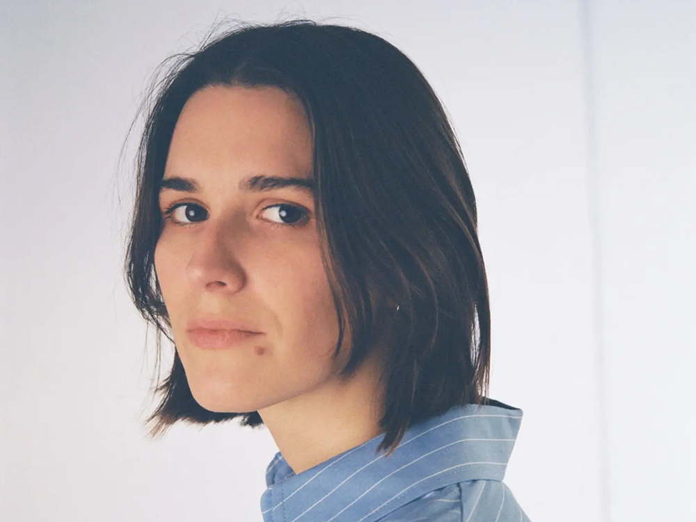 Headshot of Art School Girlfriend, a white woman with shoulder length hair and blue collared shirt