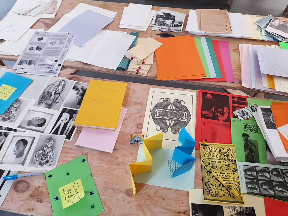Coloured paper, folded and printed leaflets, scattered across a wooden table