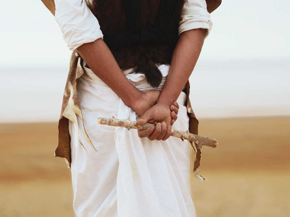 A person stands in a desert, holding a piece of branch behind their back