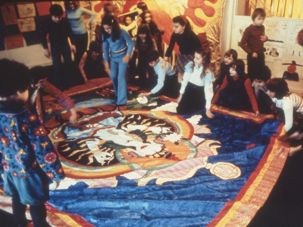 A group of school children sit around and feel a colourful tapestry by Moki Cherry