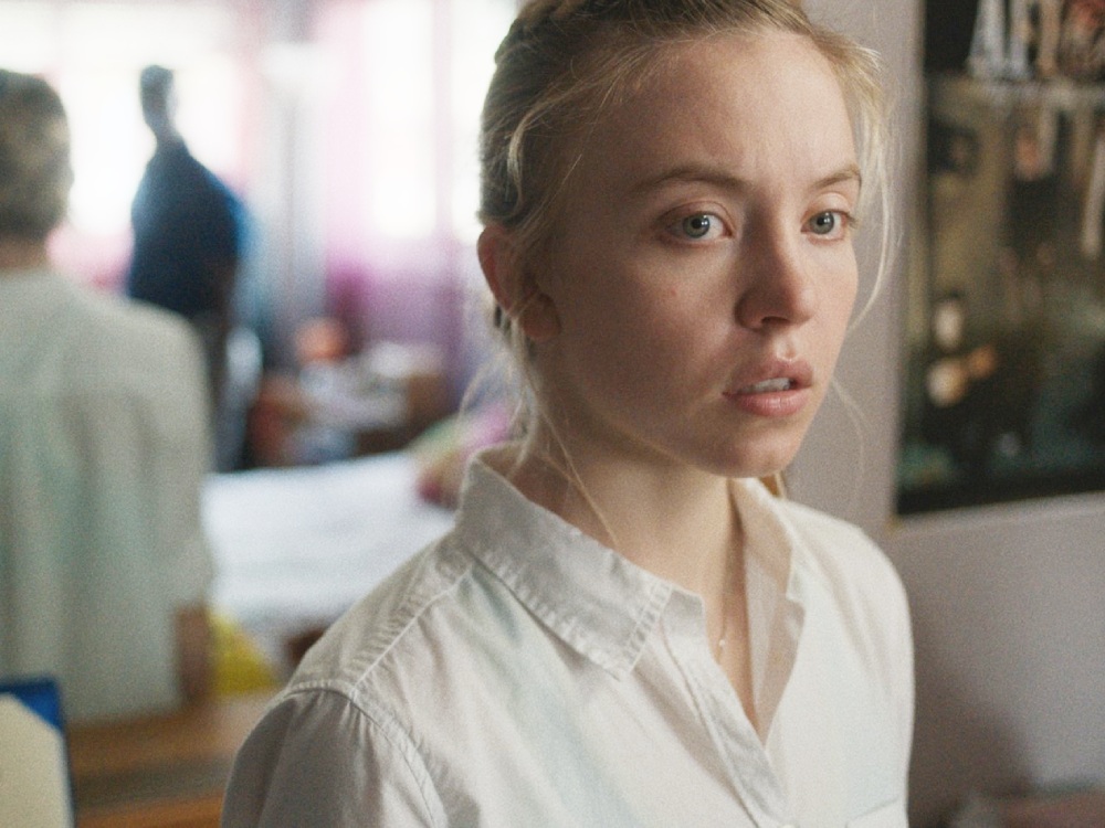 A young white woman stands in a room of her house looking off camera while the FBI raid her house