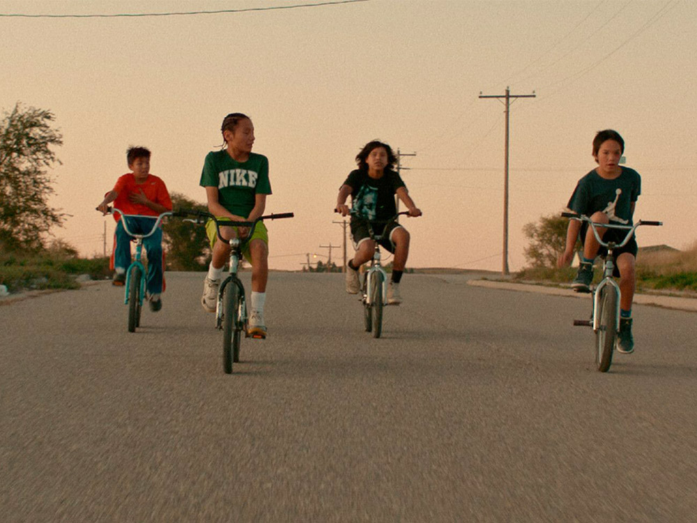 Four kids ride bikes oin a wide deserted road by sunset