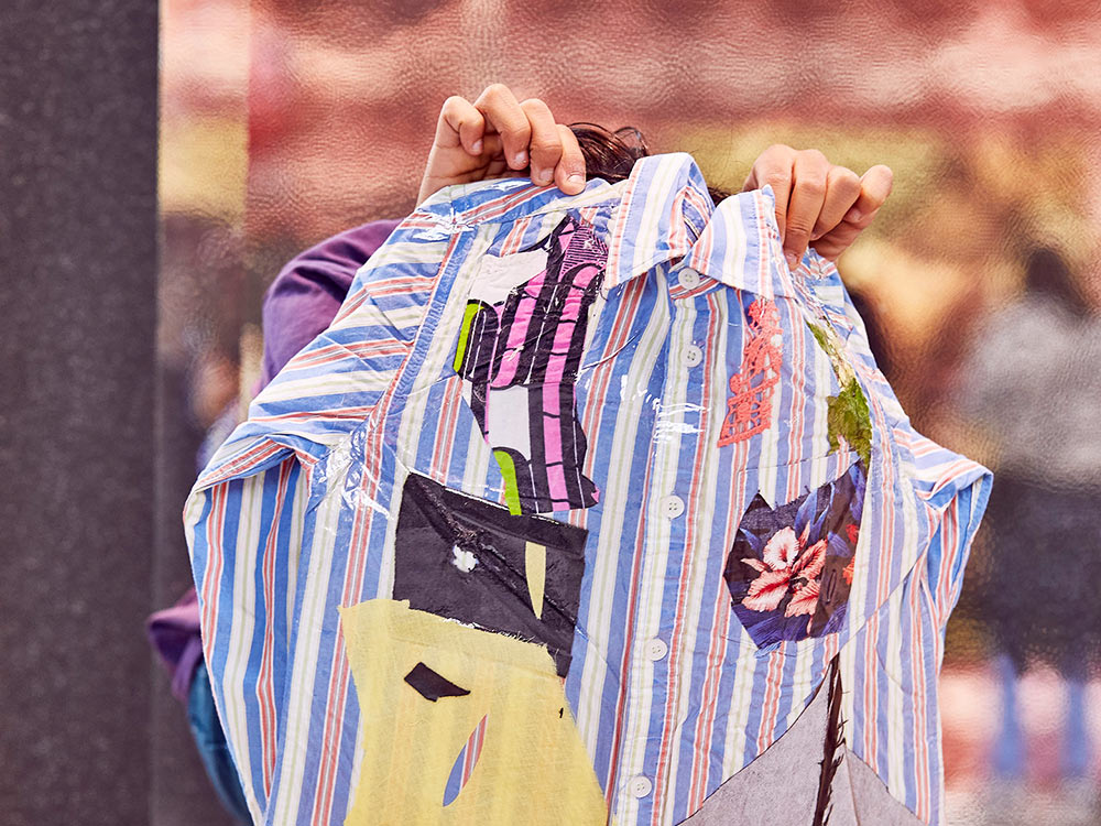 A person holds up a striped shirt patched with bright fabrics