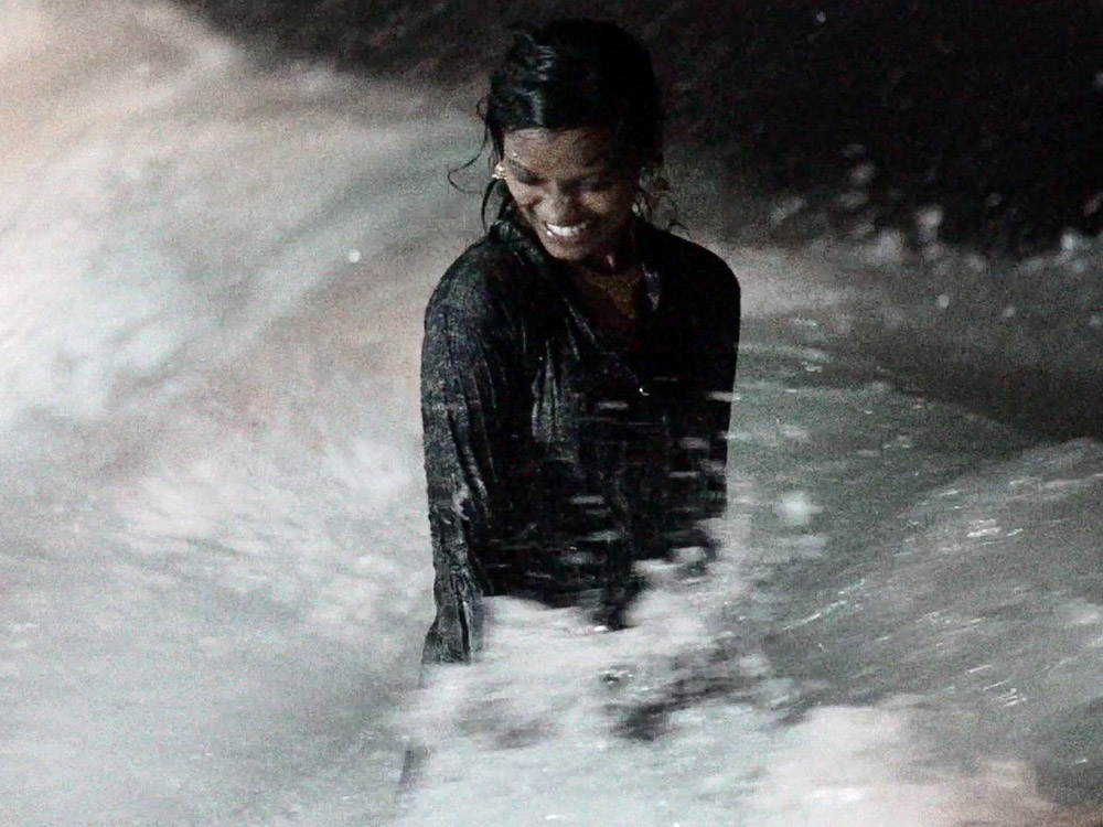 A woman stands amongst the waves at night. She's looking happy