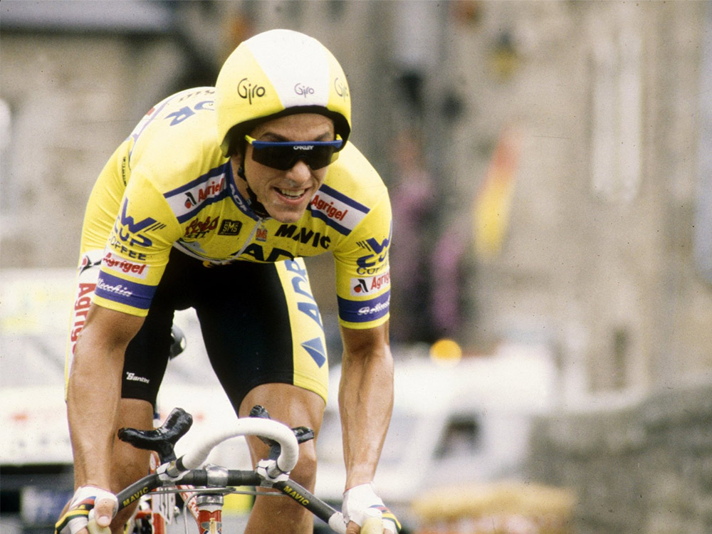 Greg LeMond in yellow racing clothes riding a race bike, hunched