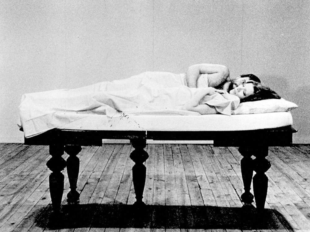 A couple lie on a mattress set on a table in the middle of an empty room
