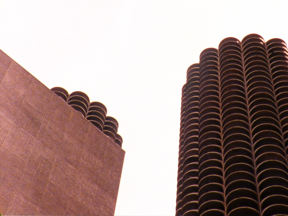 Two brutalist buildings against a bright white sky, looking like stacks of circles 