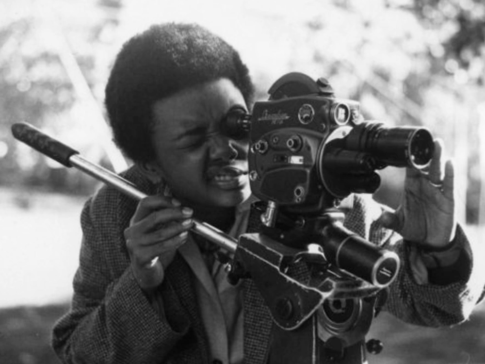A black person with short hair looks through an old camera