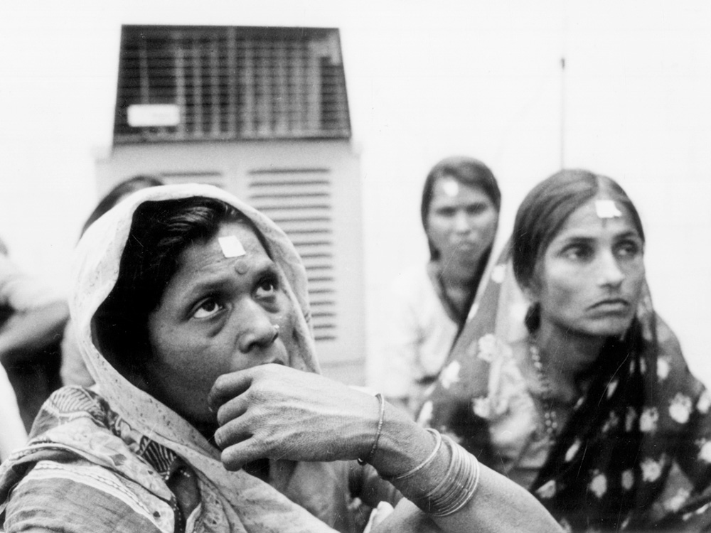 Three women watch something offscreen with tired eyes