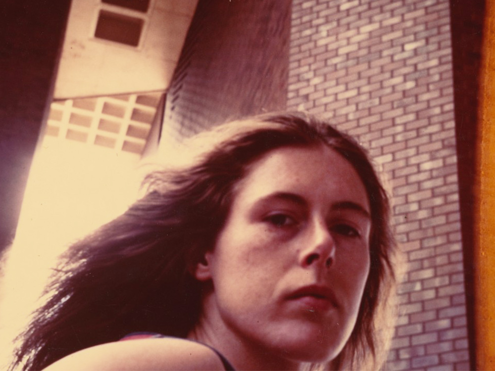 Anne Charlotte Robertson's face against a brick building stairwell. She has dark blonde flowing hair